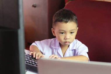 Küçük bir çocuk masada oturuyor, bilgisayar ekranına odaklanmış, teknolojiyle oynak bir öğrenme ortamında erken bir ilişki sergiliyor..