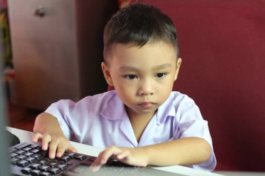 Bilgisayar kullanan, odaklanma ve konsantrasyon gösteren genç bir çocuk. Bu resim modern bir çevrede öğrenmenin ve teknolojinin özünü yakalar..