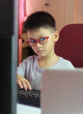 Gözlük takan genç bir çocuk ev ofis ortamında bilgisayar ekranına konsantre oluyor. Bu görüntü öğrenme ve teknolojinin özünü yakalar..