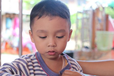 Genç bir çocuk, canlı, iç mekan ortamında bir aktiviteye derinden odaklanır. Samimi bir ifadeyle masumiyet ve merakı gözler önüne serer..