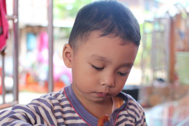 Evde atıştırmanın tadını çıkaran genç bir çocuk odaklanmış ve sakin bir ifade sergiliyor. Bu görüntü çocukluk sevincinin ve masumiyetin özünü yakalar..