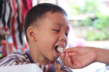 Neşeli bir çocuk açık havada atıştırmanın tadını çıkarıyor, yiyecekleri paylaşmaktan masum bir zevk alıyor. Bu görüntü çocukluk mutluluğunun ve kültürel anların özünü yakalar..