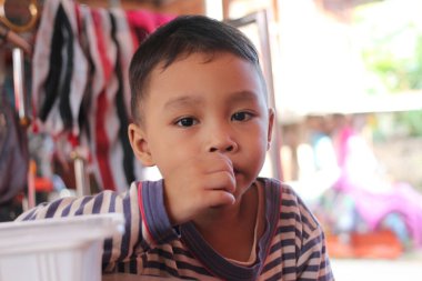 Düşüncelere dalmış, rahat ve sıcak bir ortam sunan genç bir çocuğun yakın plan portresi. Çocuğun masum ifadesi merak ve neşe saçıyor..