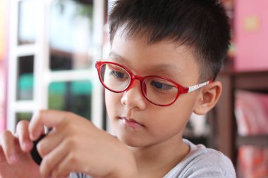 Kırmızı gözlüklü genç bir çocuk dikkatle aktif bir faaliyete odaklanıyor. Ciddi ifadesi merak ve öğrenme zevkini kapalı bir ortamda yakalıyor..