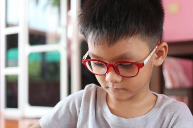 Kırmızı gözlüklü bir çocuk evde oturur, bir aktiviteye odaklanır, merakı ve yaratıcılığı somutlaştırır, evde çocukluğun sıcaklığını gösterir..