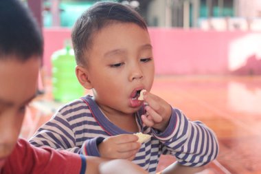 Genç bir çocuk, keyifli bir ifade sergileyerek evde lezzetli bir şeyler atıştırmaktan hoşlanır. Bu hareketli ortam, çocukluk anılarının neşeli atmosferine ekleniyor..