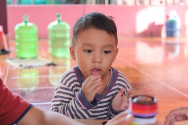 Genç bir çocuk, renkli oyuncaklarla etkileşime girerken, merakını ve dikkatini gösteren, evde oyun zamanı aktivitesiyle derinden ilgilenir. Sıcak ortam, çocukluk keşiflerinin neşeli atmosferini arttırır..