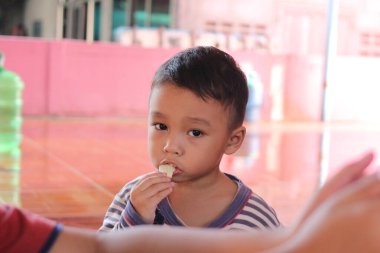 Genç bir çocuk iyi aydınlatılmış kapalı bir ortamda atıştırmanın tadını çıkarıyor. Onun tuhaf ifadesi çocukluk sevincini ve masumiyetini yakalar..