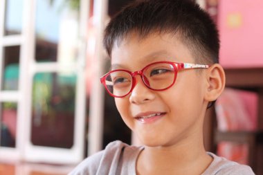 Kırmızı gözlüklü neşeli bir çocuk sıcak bir iç mekanda ışıl ışıl gülümsüyor. Bu neşeli portre çocukluk ve mutluluğun özünü yansıtıyor..