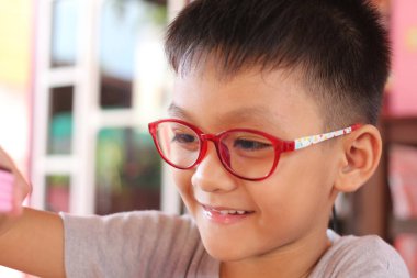 Kırmızı gözlüklü neşeli bir çocuk oyun oynarken gülümsüyor. Bu yakın plan portre, eğitim ve yaratıcılık temaları için mükemmel olan çocukluğun neşe ve masumiyetini yansıtıyor..