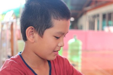 Kırmızı tişörtlü genç bir çocuk bir aktivite sırasında konsantrasyonunu gösterir. Samimi an, çocukluk masumiyetini ve merakını sıcak ve davetkar bir ortamda yakalar..