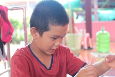 Kırmızı tişörtlü odaklanmış bir çocuk, yaratıcı bir aktiviteye girişir, hayal gücünü keşfederken konsantrasyon ve neşe gösterir..