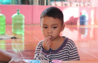 Düşünceli genç bir çocuk, oyuncaklarla dolu renkli bir ortamda, eğlenceli bir aktiviteye katılır, konsantrasyon ve merak gösterir..