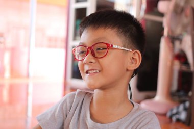 Gözlüklü mutlu bir çocuk evde otururken sıcak bir şekilde gülümser. Neşeli ifade onun neşeli doğasını yansıtıyor, o ana masumiyet katıyor..