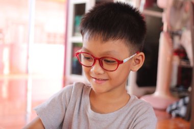 Kırmızı gözlüklü genç bir çocuk evde faaliyet gösterirken gülümsüyor. Neşeli atmosfer çocukluk sevincinin ve masumiyetin özünü yakalar..