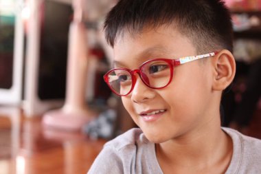 Renkli gözlük takan neşeli bir çocuk kapalı bir ortamda sıcak bir şekilde gülümser, çocukluk sevincinin ve merakının özünü şakacı bir anda yakalar..