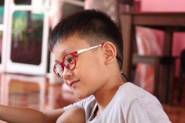 Kırmızı gözlük takan genç bir çocuk evde oturur, odaklanma ve yaratıcılık duygusu taşır. Renkli arkaplan bu samimi ana sıcaklık katar.