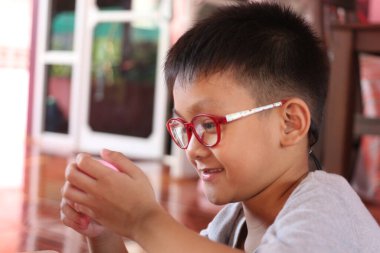 Gözlüklü neşeli bir genç çocuk yaratıcı bir faaliyete odaklanır. Neşeli ifadesi ve şakacı tavırları mutluluk ve bağlılık anını içeride yakalıyor..