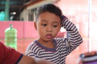 Çizgili tişörtlü düşünceli genç bir çocuk. Kapalı bir etkinlikle meşgul olurken dalgın görünüyor. Çocukluk merakı ve masumiyetini yakalıyor..