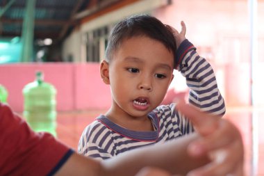 Genç bir çocuk, çocukluk keşiflerinin neşesini ve masumiyetini gösteren, kapalı alanlarda eğlenceli bir aktivite yaparken tuhaf bir ifade sergiliyor..