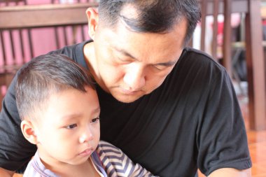 Bir baba ve oğlu arasındaki dokunaklı bir an sevgi ve şefkat göstergesi. Kapalı alan ayarları derin bağlarını ve duygusal bağlantılarını vurguluyor..