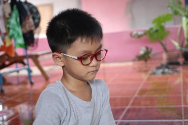 Gözlüklü genç bir çocuk düşünceli bir şekilde içeride oturur, masumiyetini ve merakını gösterir. Rahatlatıcı ayar çocukluktaki bir anlık tefekkür görüntüsünü yakalar..