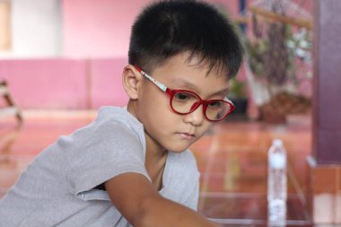 Kırmızı gözlük takan düşünceli bir çocuk, canlı bir ortamda konsantrasyon ve merakını gösteren yaratıcı bir aktiviteye girişiyor. Çocukluk ve öğrenim temaları için mükemmel.