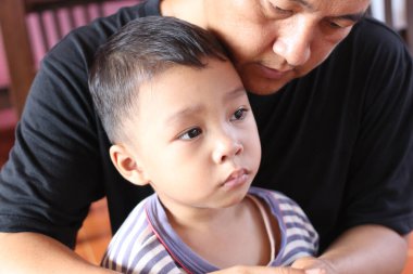 Bir baba ve oğul arasındaki dokunaklı bir an derin bağlarını ve sevgilerini gösteriyor. Görüntü, aile sevgisini ve çocukluğun sıcaklığını yansıtıyor..