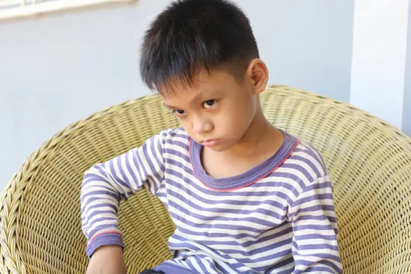 Çizgili pijamalı düşünceli bir çocuk koltuğa rahatça oturur ve çocukluk duygularının ve boş zamanlarının özünü yansıtan samimi bir ifade sergiler..