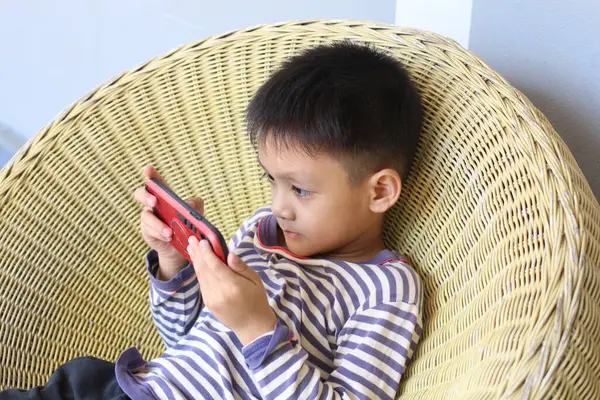 Küçük bir çocuk rahat rahat rahat rahat rahat rahat rahat rahat rahat rahat bir oyun oynamaya odaklanır. Sahne, modern teknolojinin gelişigüzel bir ortamda eğlencesini ve bağlılığını yakalıyor..