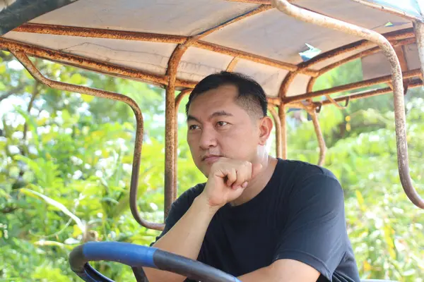 Düşünceli bir adam canlı yeşilliklerle çevrili taşralı bir araçta oturuyor. Dalgın görünüyor, doğadaki huzurlu anın tadını çıkarıyor..