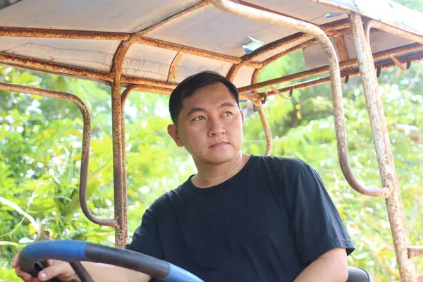 Dalgın bir adam yemyeşil bir araziyle çevrili kırsal bir araçta oturuyor. Onun düşünceli ifadesi sakin bir anı yakalıyor, doğayı ve içgözlem duygusunu harmanlıyor..