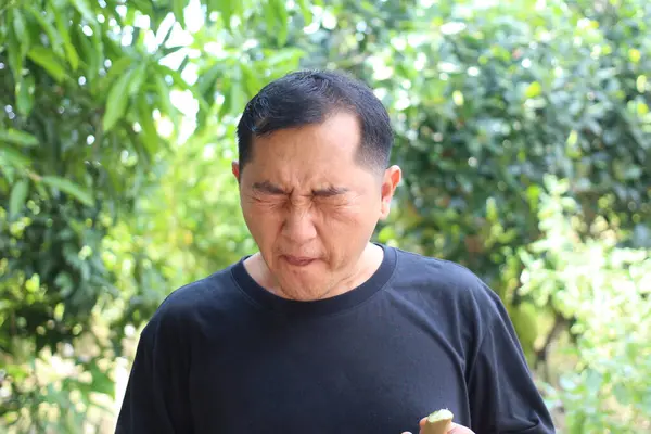 Açık havada bir adam komik bir ifade sergiliyor, şaşırtıcı bir tat alıyor. Yeşilliklerle çevrili, doğada samimi duygular barındırıyor..