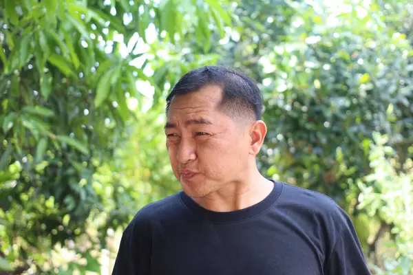 Düşünceli bir adam açık havada, yemyeşil bir ortamda, canlı doğal bir arka plana karşı sakin bir ifade sergiliyor. Yaşam tarzı temaları için mükemmel.