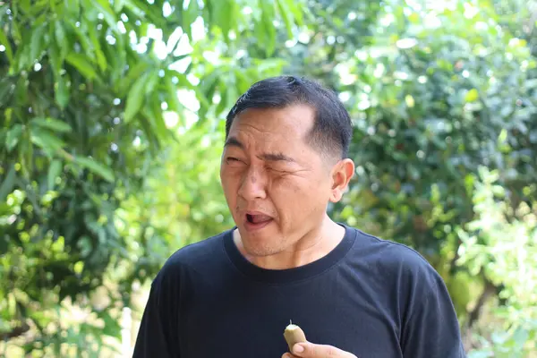 Bir adam canlı yeşil bir manzaranın ortasında atıştırmanın tadını çıkarıyor. Neşeli ifadesi, doğadaki eğlence ve zevkin özünü yakalıyor..