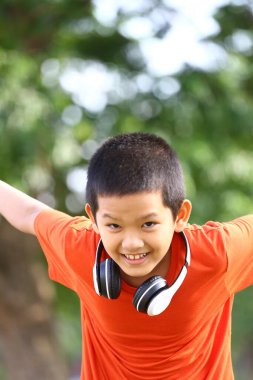 Kulaklık takan neşeli bir çocuk dışarıda güneşli bir günün tadını çıkarıyor. Doğayla iç içe eğlenirken neşe ve özgürlüğü ifade ediyor..