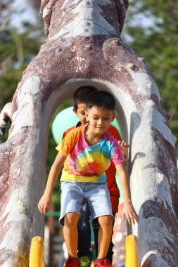 İki çocuk oyun parkında kaymaktan keyif alır. Neşelerini ve dostluklarını açık havada gösterirler. Eğlenceli aktiviteler için mükemmel bir ortam..