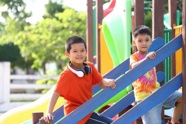 İki neşeli çocuk oyun parkındaki renkli ekipmanlara binip eğleniyor ve arkadaşlığı desteklerken neşeli anılar yaratıyorlar..