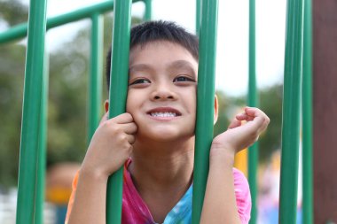 Neşeli bir çocuk oyun parkında eğleniyor, neşe ve mutluluk sergiliyor renkli yeşil parmaklıkların arasından bakıyor. Çocukluk anılarını yakalamak için mükemmel..