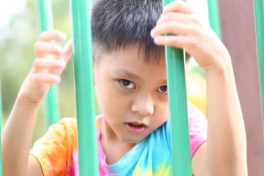 Çocuk parkındaki renkli çubuklar arasında neşeli bir ifadeye sahip küçük bir çocuk, neşe ve kaygısız çocukluk keşfi ruhunu yakalıyor..