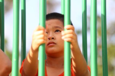 Genç bir çocuk oyun alanı ekipmanlarıyla etkileşime geçiyor, merak ve neşe sergiliyor. Görüntü, parlak güneş ışığında çocukluk macerasının bir anını yakalıyor..