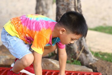 A joyful child wearing a colorful tie-dye shirt plays outdoors. The boy climbs on playground equipment, showcasing his carefree spirit and summer happiness. clipart