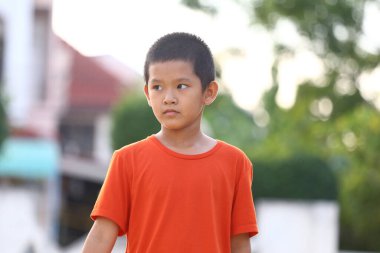 Turuncu gömlek giyen kendine güvenen bir çocuk dışarıda durup bir anlık tefekkür görüntüsü yakalıyor. Odaklanmış bakışları ve günlük tarzı gençliği ve kişiliğini yansıtıyor..