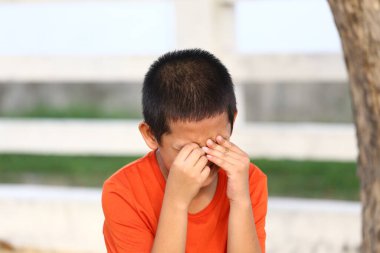 Turuncu gömlekli genç bir çocuk duygularını elleriyle gözlerini kapatarak dışardaki bir ortamda üzüntü ya da hüsran anlarını resmederek gösterir..