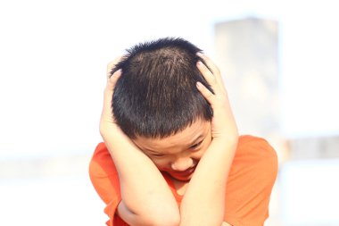 Sıkıntılı bir ifadeye sahip genç bir çocuk, kulaklarını kapatıyor, çocukluk duygularının özünü ve gençliğin masumiyetini samimi bir anda yakalıyor..