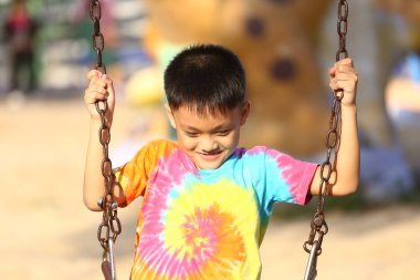 Neşeli bir çocuk, canlı bir kravat boyası tişört giyerek salıncakta sallanmaktan hoşlanır. Günışığı sahnesi mutluluğun ve kaygısız çocukluk anlarının özünü yakalar..
