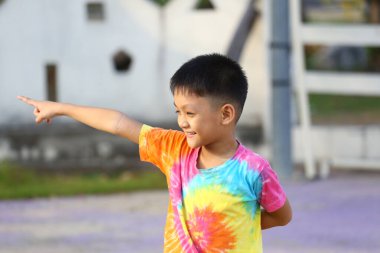 Renkli bir kravat boyası tişört giyen neşeli bir çocuk heyecan verici bir şekilde mutluluk ve kaygısız çocukluk ruhunu açık hava ortamında somutlaştırıyor..