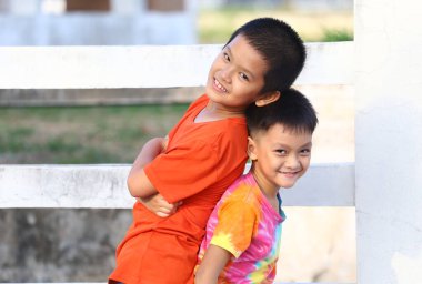 İki neşeli çocuk açık havada neşeli bir anın tadını çıkarıyorlar. Güneşin altında beyaz bir çite yaslanarak çocukluk masumiyetinin özünü yakalıyorlar..