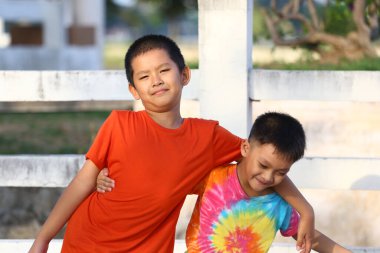 İki neşeli çocuk açık havada güneşli bir arka planda canlı tişörtler sergileyerek eğleniyorlar. Onların neşeli ifadeleri gerçek dostluğu ve sevinci yansıtır..