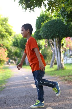 Neşeli bir çocuk yeşil bir parkta manzaralı bir yolda koşuyor, dışarıda zaman geçirmekten zevk alıyor. Canlı kıyafetleri onun neşeli ruhunu ve kaygısız doğasını yansıtıyor..